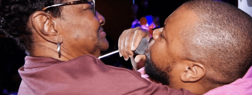 Man hugging woman while singing on stage.